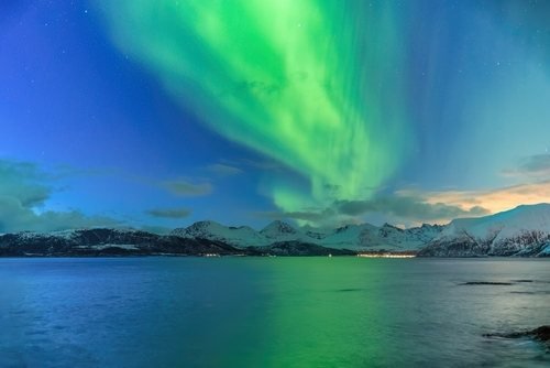 Grüne Polarlichter über verschneiten Bergen und dem Meer