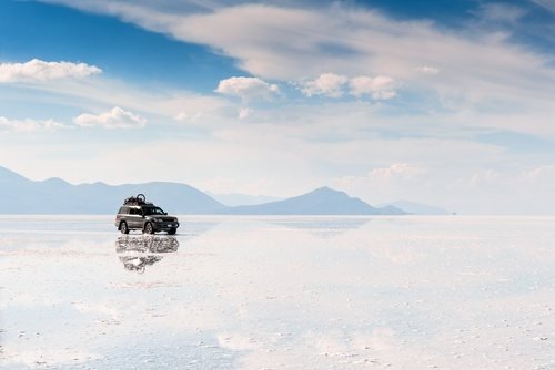 Geländewagen auf dem nassen Salzsee, der Himmel und Wolken spiegelt